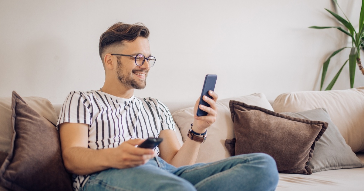 man using tv remote and cell phone